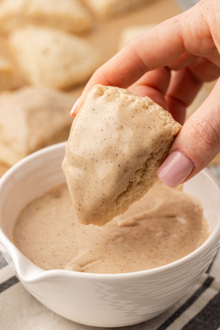 A vanilla bean scone being lifted from a bowl of icing.