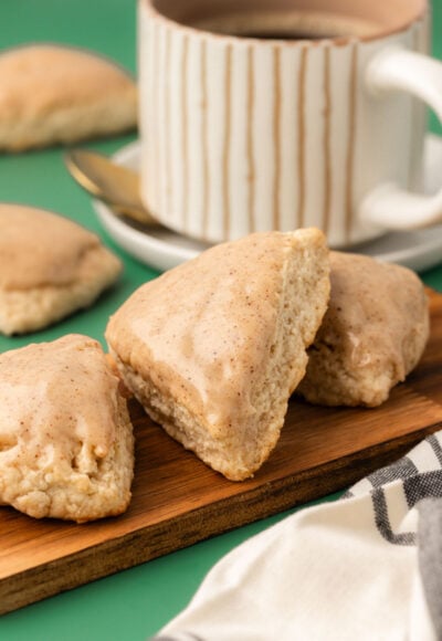 Three vanilla scones on a small wooden board with a mug of coffee in the background.