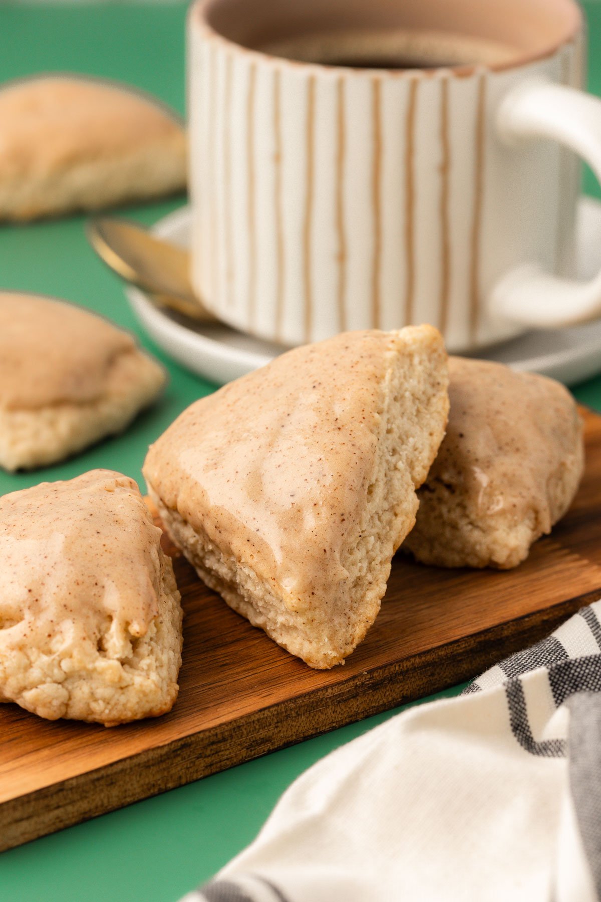 Three vanilla scones on a small wooden board with a mug of coffee in the background.