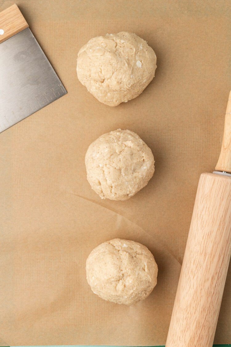 Dough for scones divided into three balls on parchment paper.
