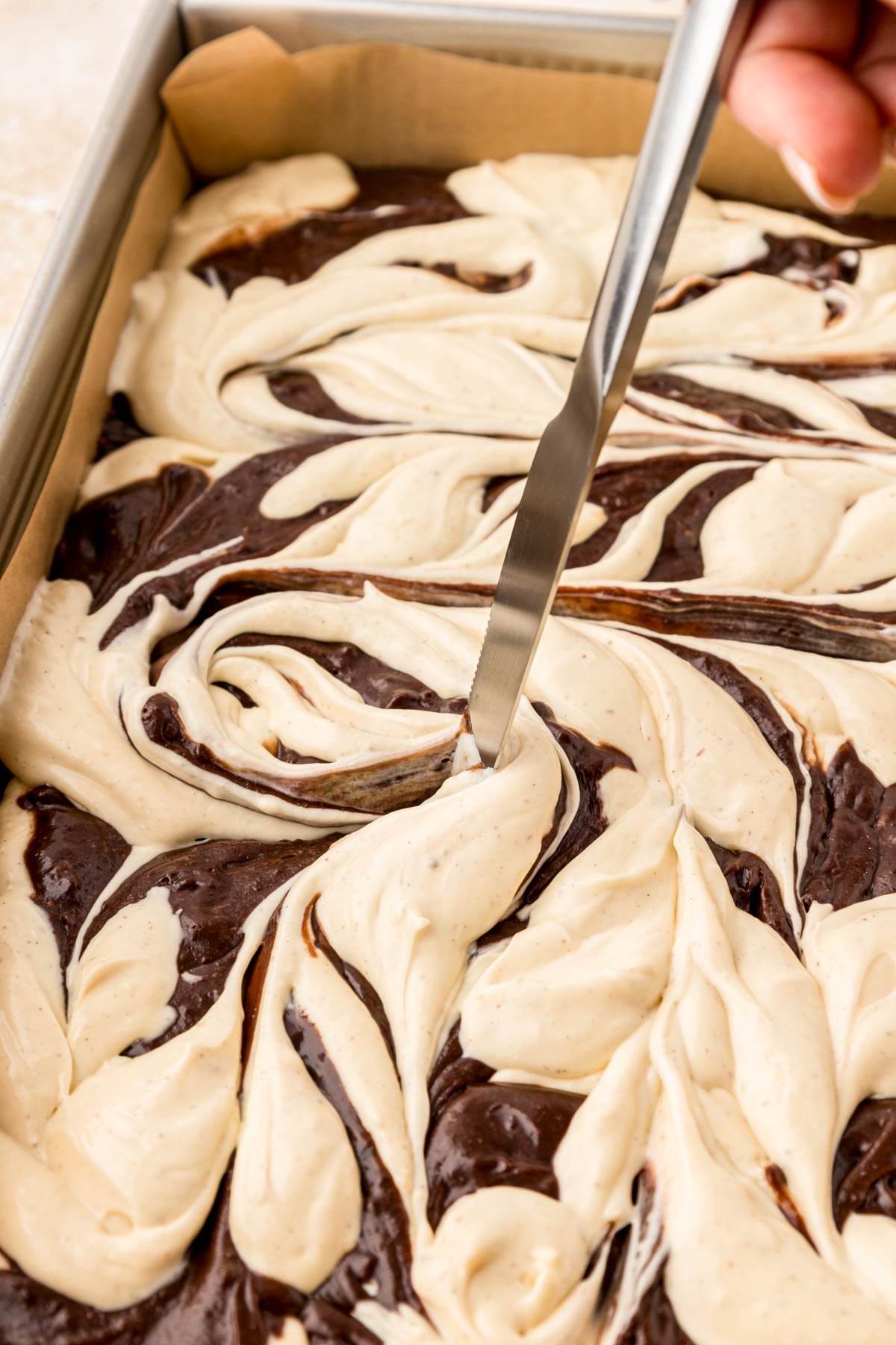 Close up of a knife swirling brownie and cheesecake batter together.