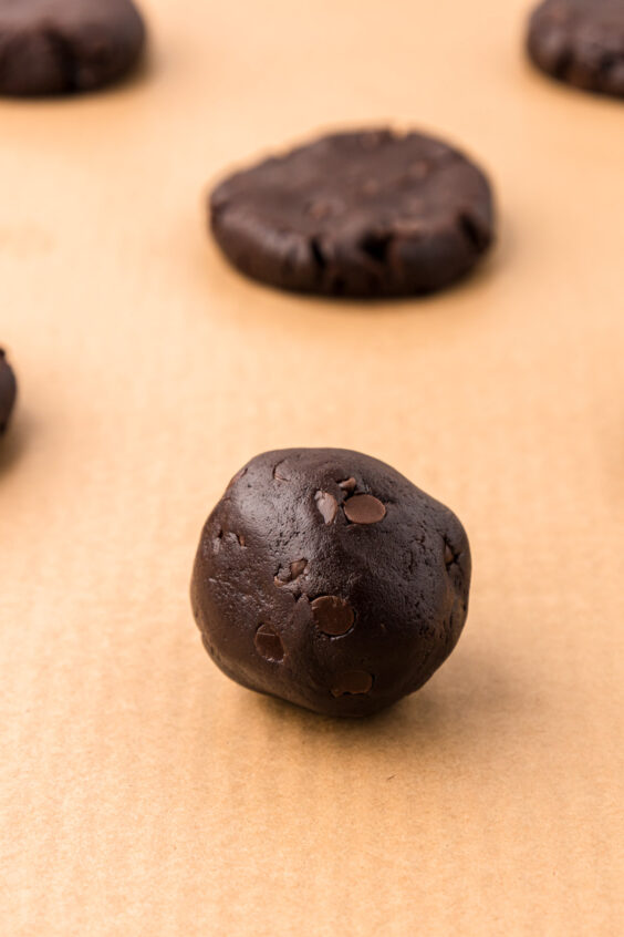 Balls of chocolate cookie dough on parchment lined baking sheet.