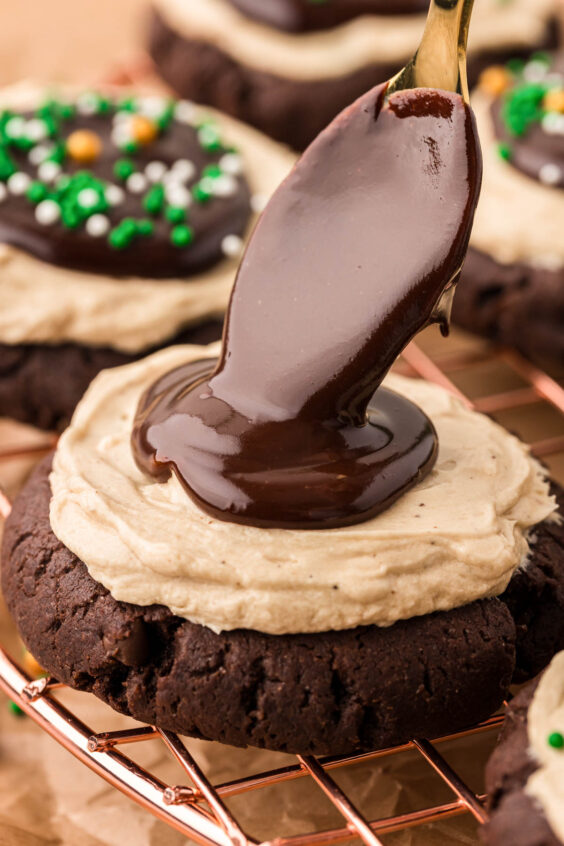 Chocolate ganache being spooned onto a frosted cookie.