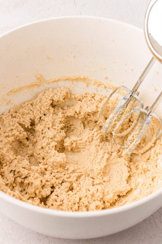 Butter and sugar being creamed by a hand mixer in a bowl.