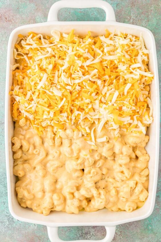 mac and cheese and extra shredded cheese being layered in a baking dish.