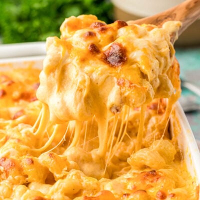 A serving spoon scooping mac and cheese out of a casserole dish.