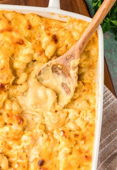 Overhead of a wooden spoon scooping mac and cheese out of a casserole dish.