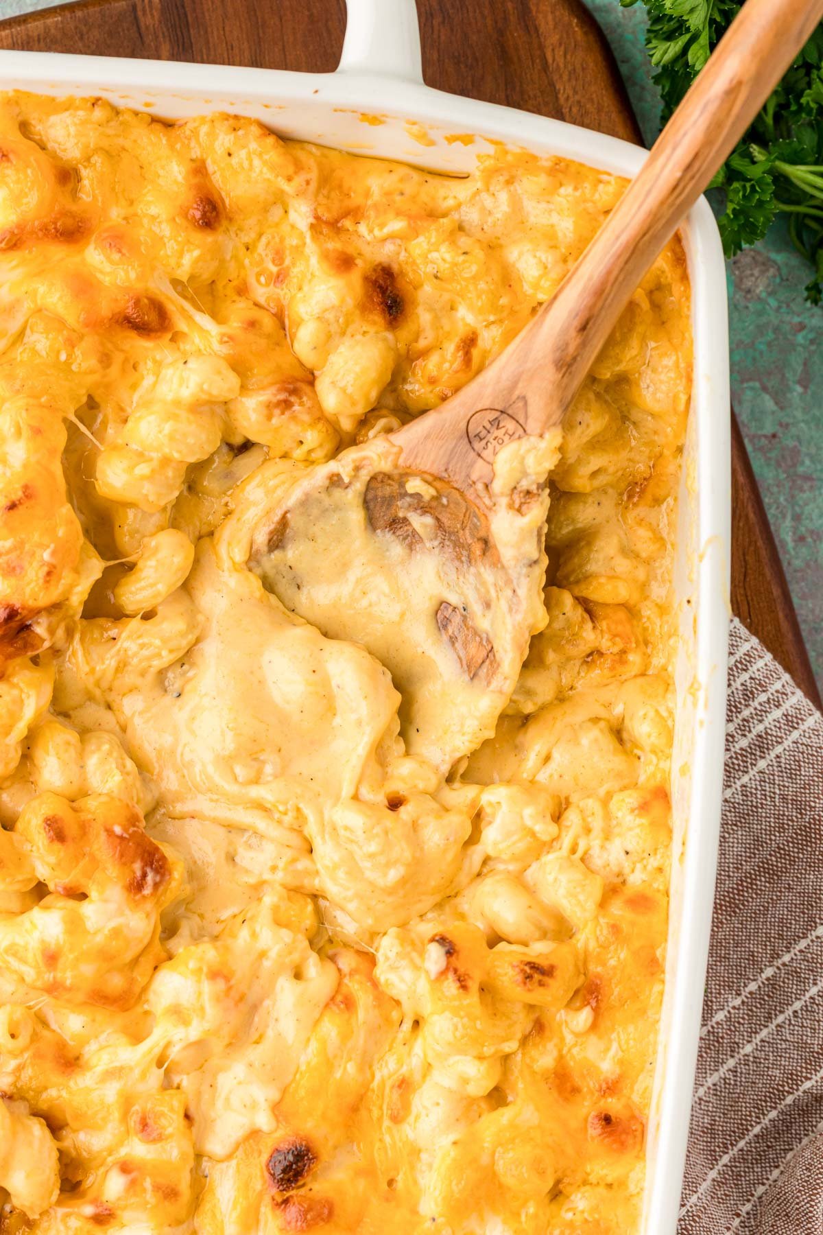 Overhead of a wooden spoon scooping mac and cheese out of a casserole dish.