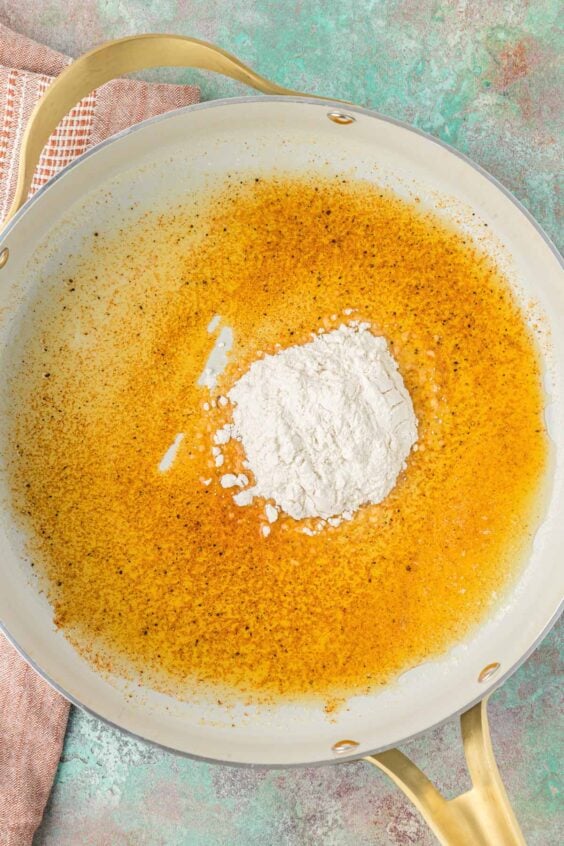 Flour being added to melted butter and spices to make a roux.