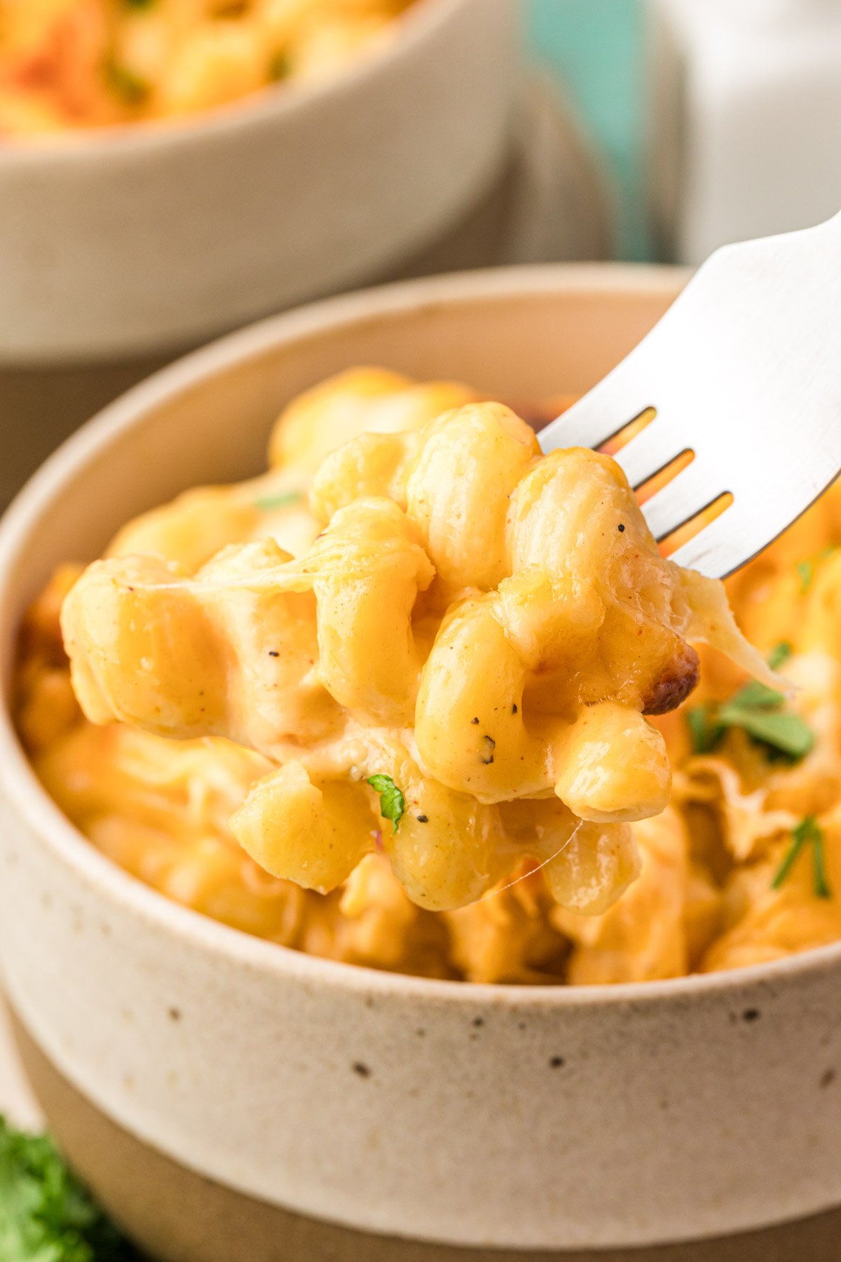 A fork scooping a bite of mac and cheese out of a bowl.