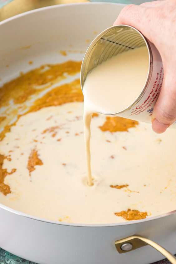 Evaporated milk being added to a roux to make mac and cheese sauce.