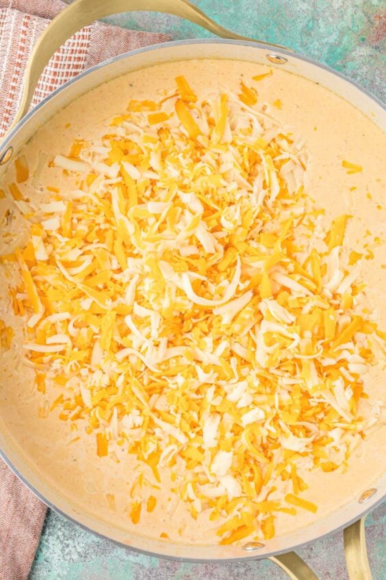 Shredded cheese being added to cream sauce for mac and cheese.