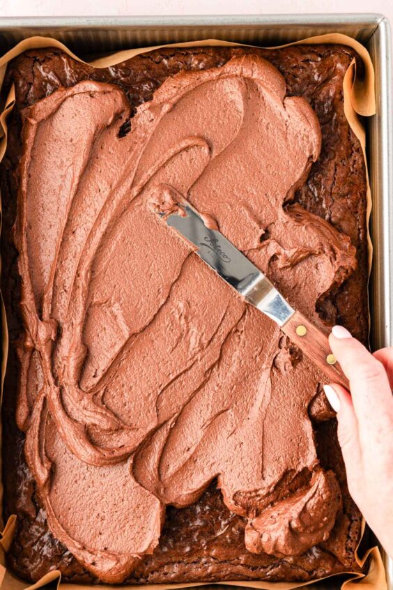 Frosting being spread over the top of brownies.