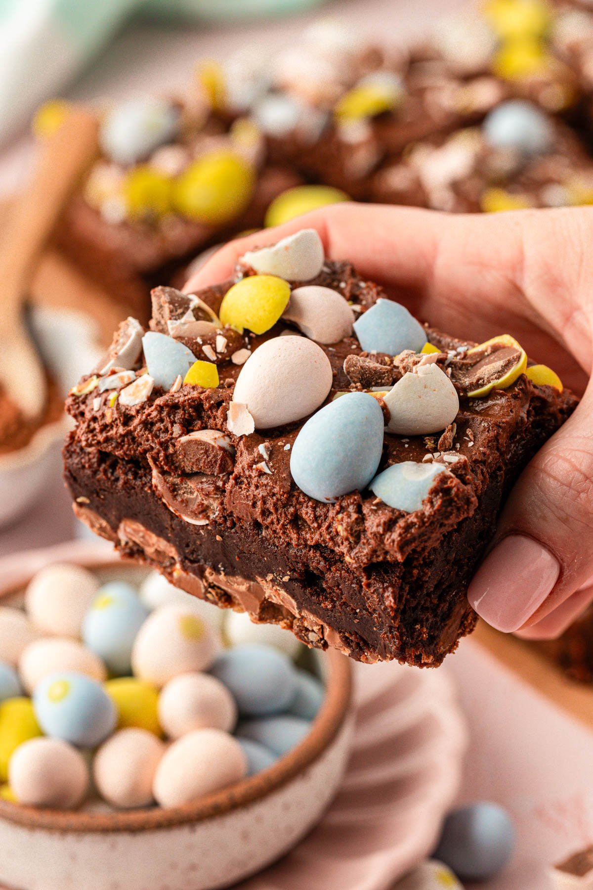 A woman's hand holding a cadbury mini egg brownie to the camera.