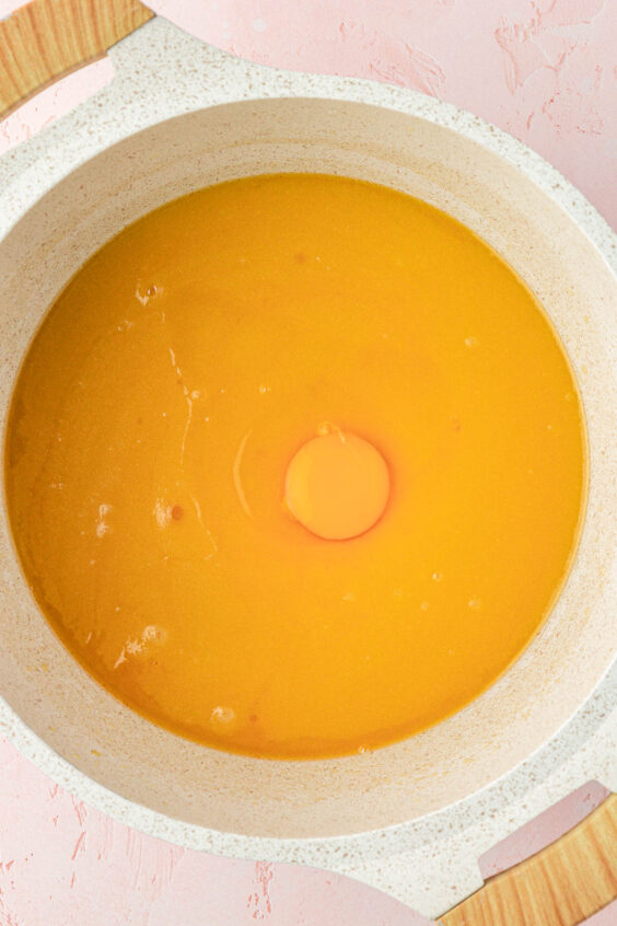 Egg being added to a pot of sugar and butter.