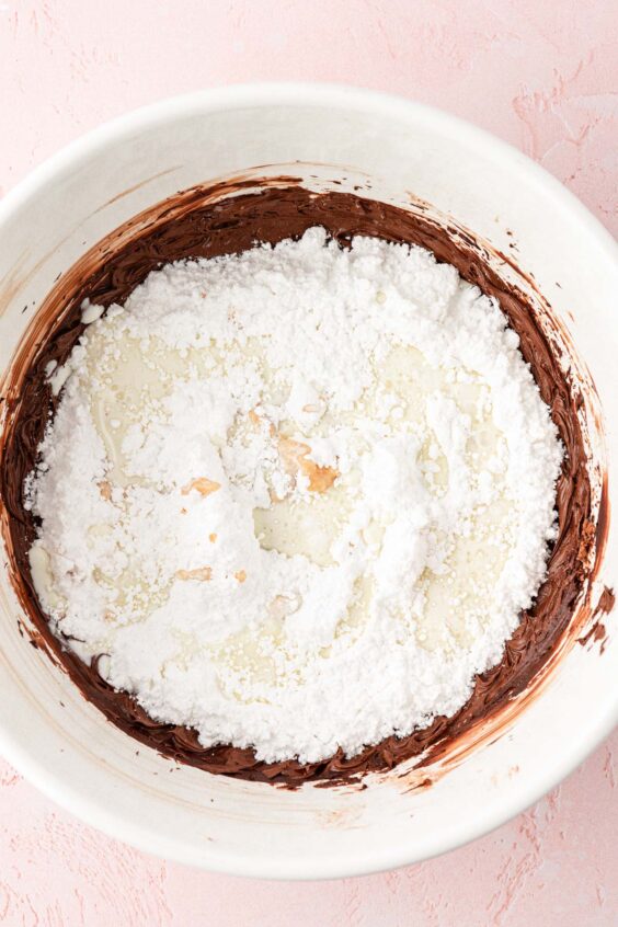 Powdered sugar and cream being added to a bowl to make chocolate frosting.