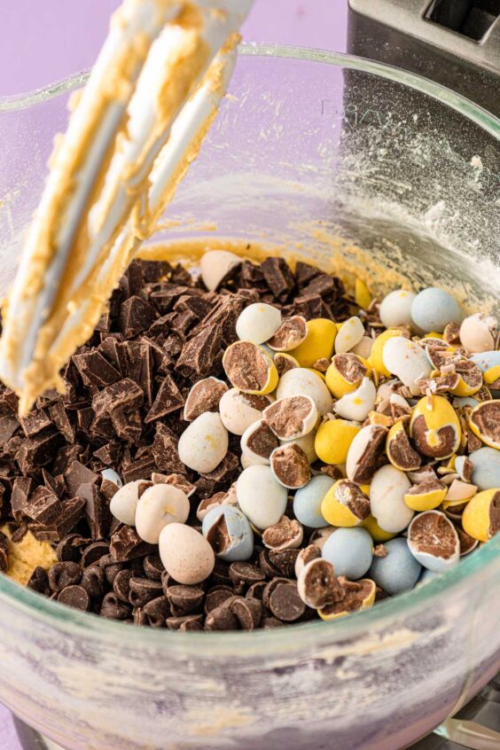 Chocolate and chopped Cadbury eggs being added to cookie dough in a mixer.