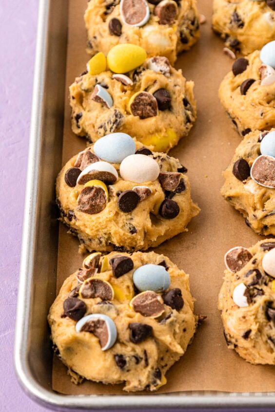 Cadbury mini eggs on cookie dough balls on a baking pan.