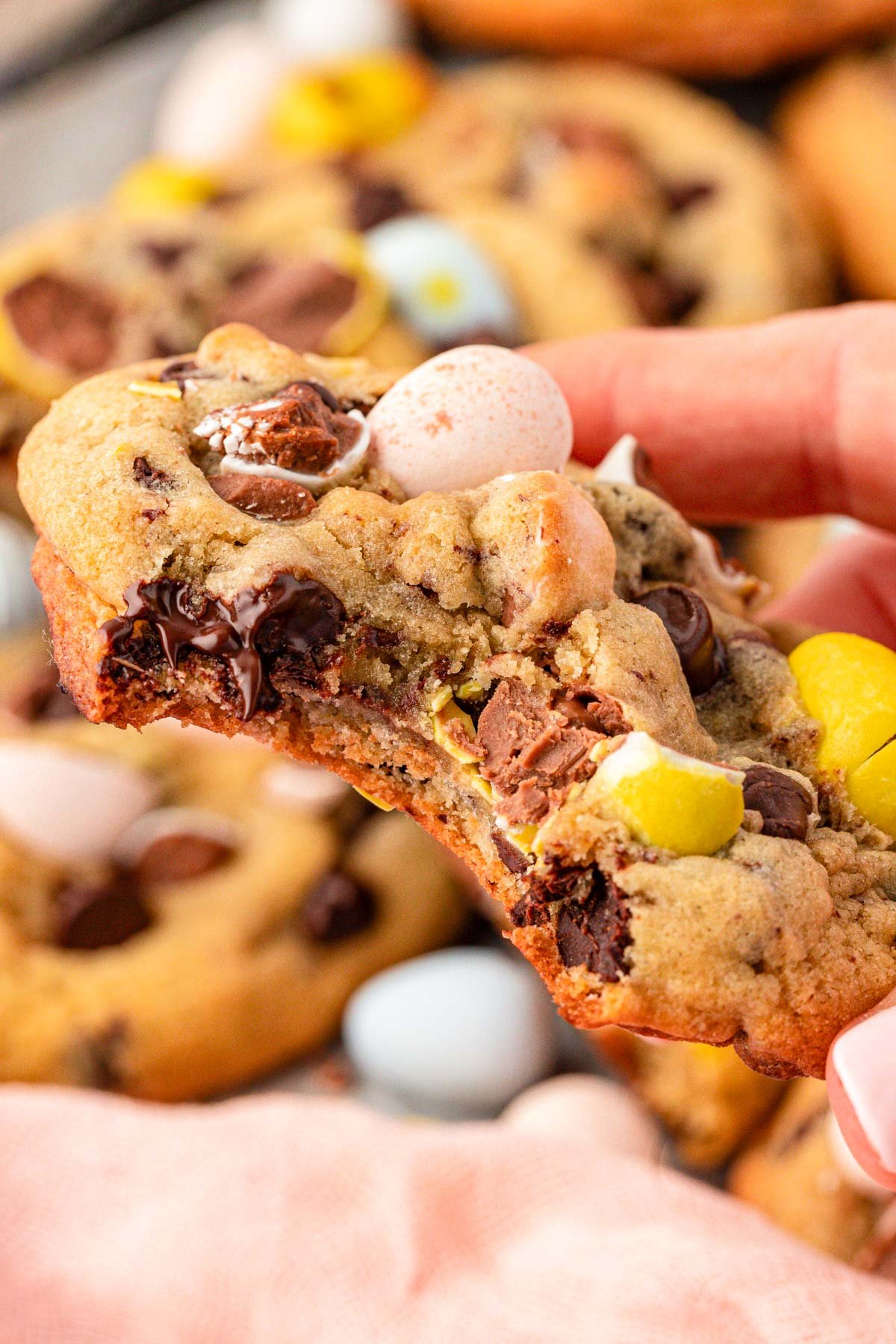 A woman's hand holding a Cadbury Chocolate Chip Cookie to the camera. 