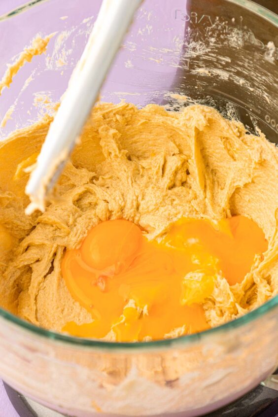Eggs being added to a mixing bowl to make cookie dough.