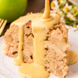 Vanilla custard being poured on Irish Apple Cake slice on a white plate.