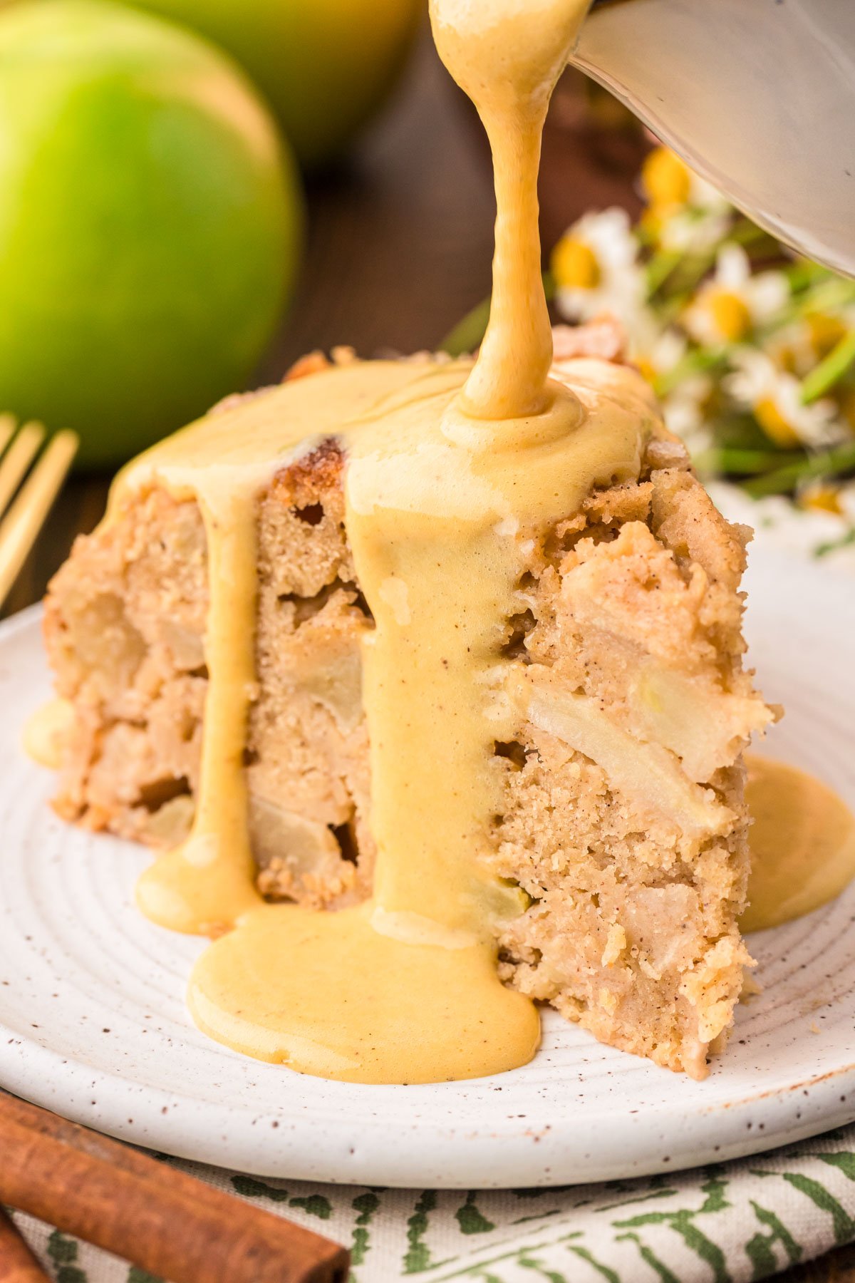 Vanilla custard being poured on Irish Apple Cake slice on a white plate.