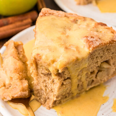 A slice of Irish Apple Cake on a white plate with a fork with a bite on it.