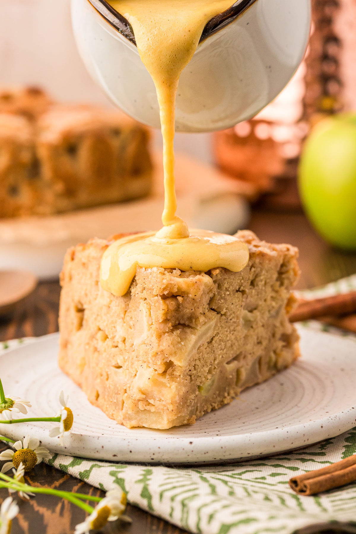 Vanilla custard being poured on Irish Apple Cake slice on a white plate.