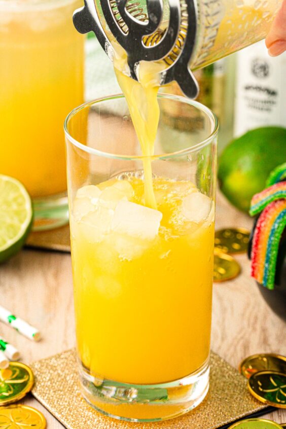 A drink being strained into a glass with ice.