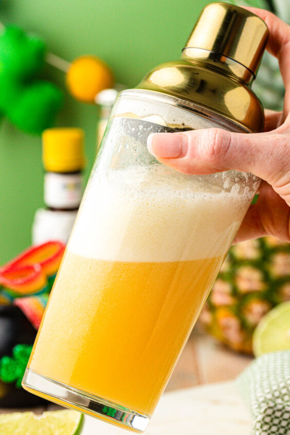 A cocktail shaker shaking a yellow mocktail.