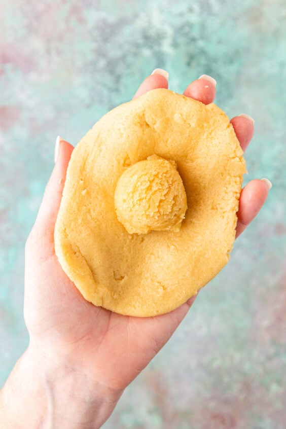 A woman's hand holding cookie dough ready to be wrapped around a ball of frangipane.