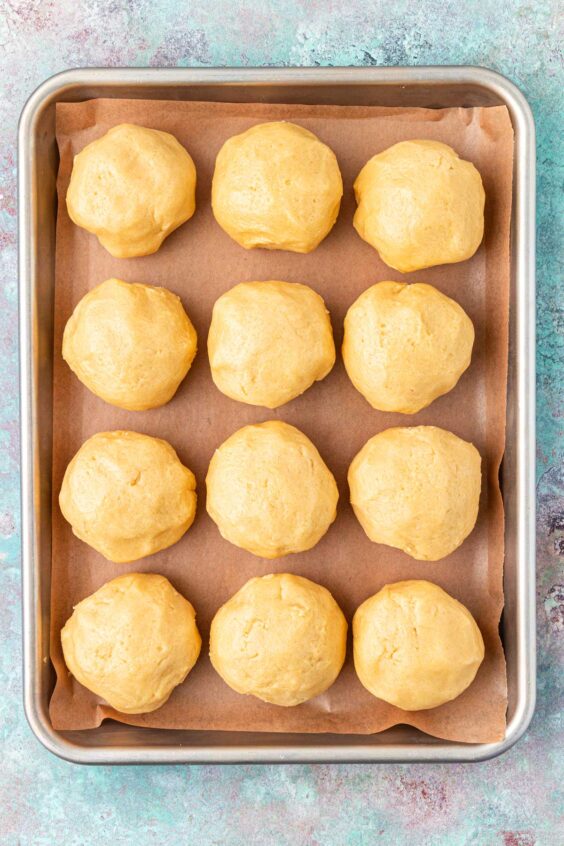 Balls of almond cookie dough on a parchment lined baking sheet.