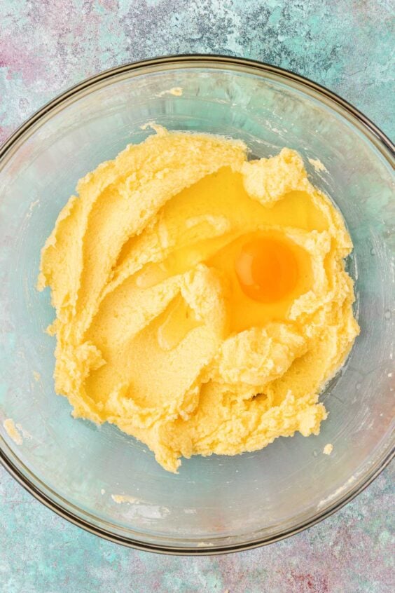 Egg being added to creamed butter and sugar in a mixing bowl.