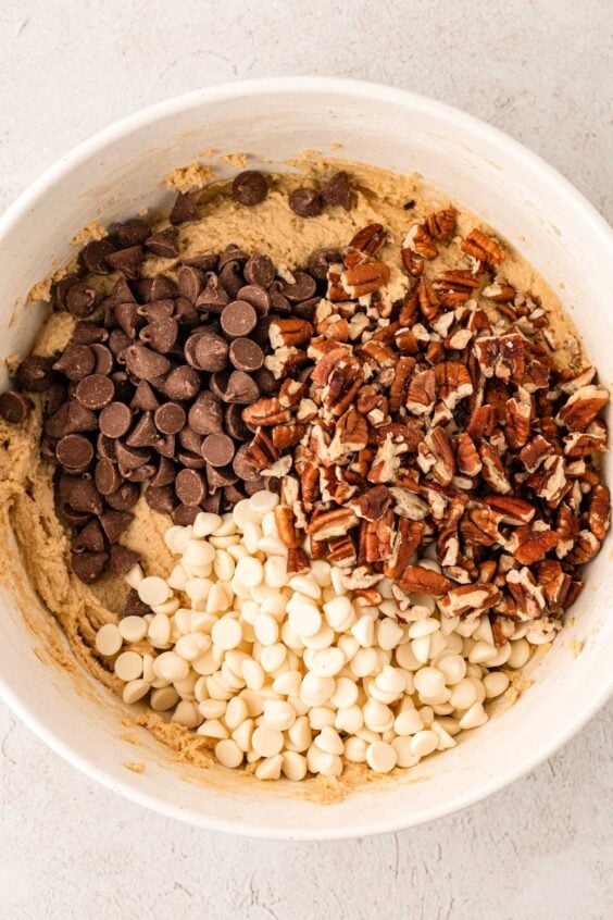 Chocolate chips and pecans being added to a bowl of cookie dough.