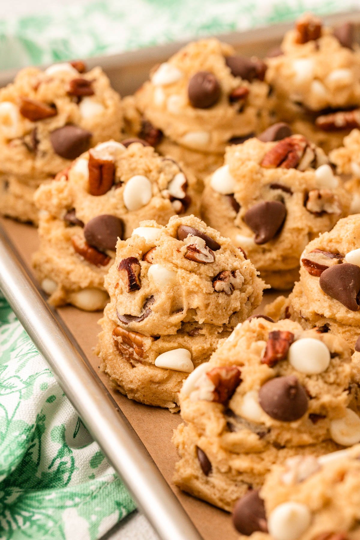 Scoops of cookie dough with pecans and chocolate chips on a baking sheet.