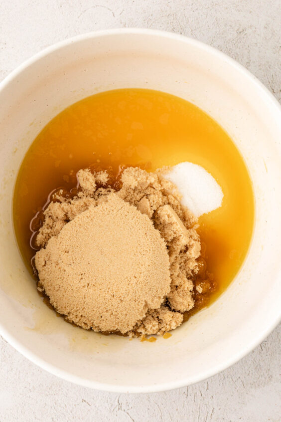 Sugar being added to melted butter in a white bowl.