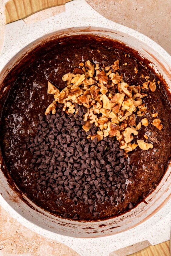 Chocolate chips and walnuts being mixed into a pot of brownie batter.