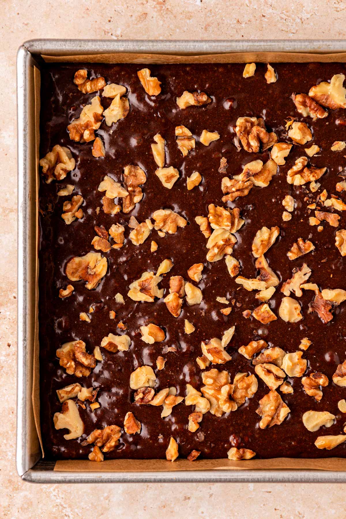 Close up of brownie batter in a pan topped with walnuts.