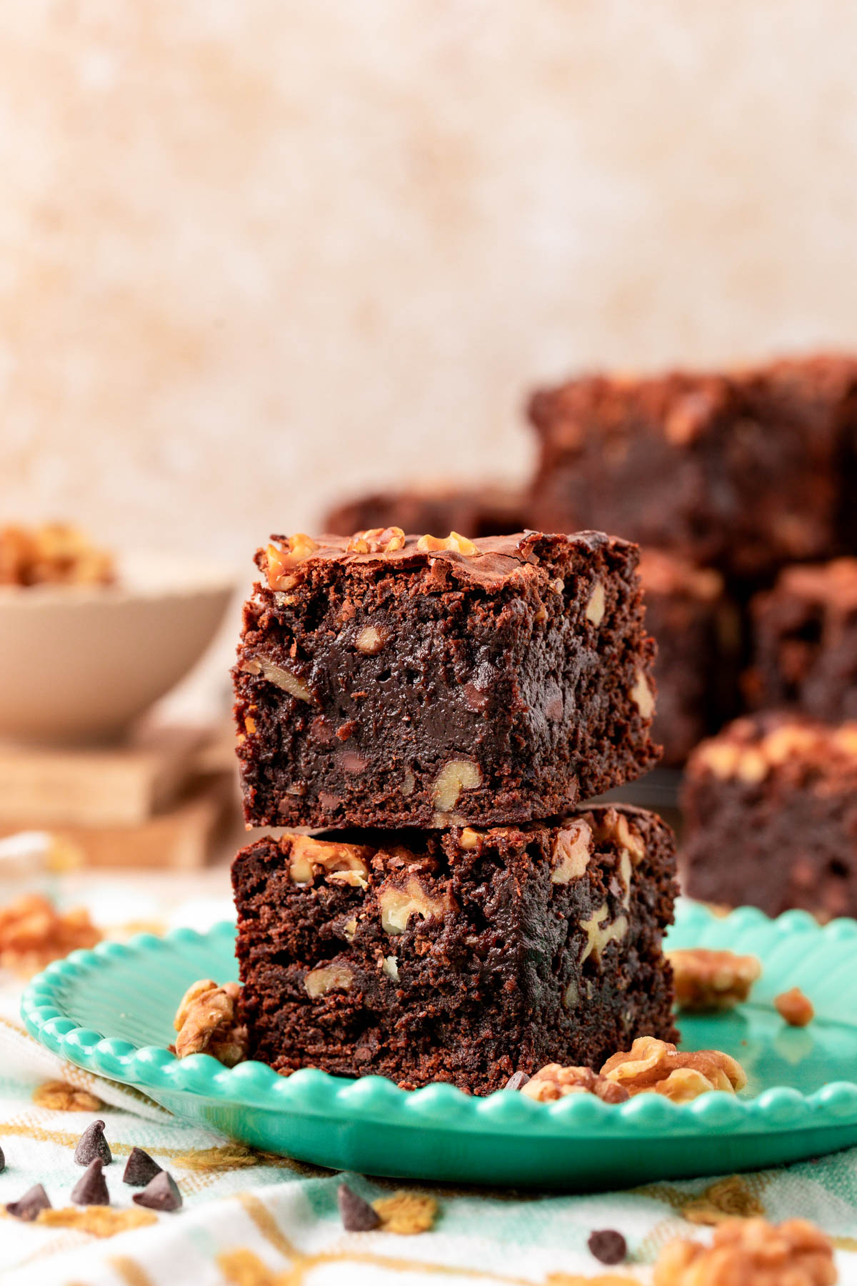 Two walnut fudge brownies stacked on a teal plate.