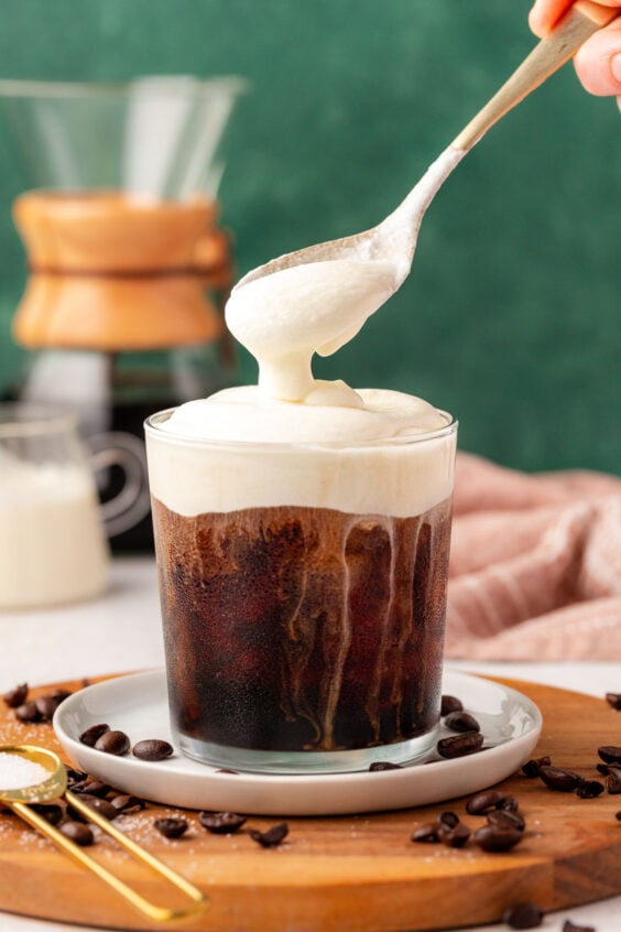 Cold foam being spooned on top of a cup of iced coffee.