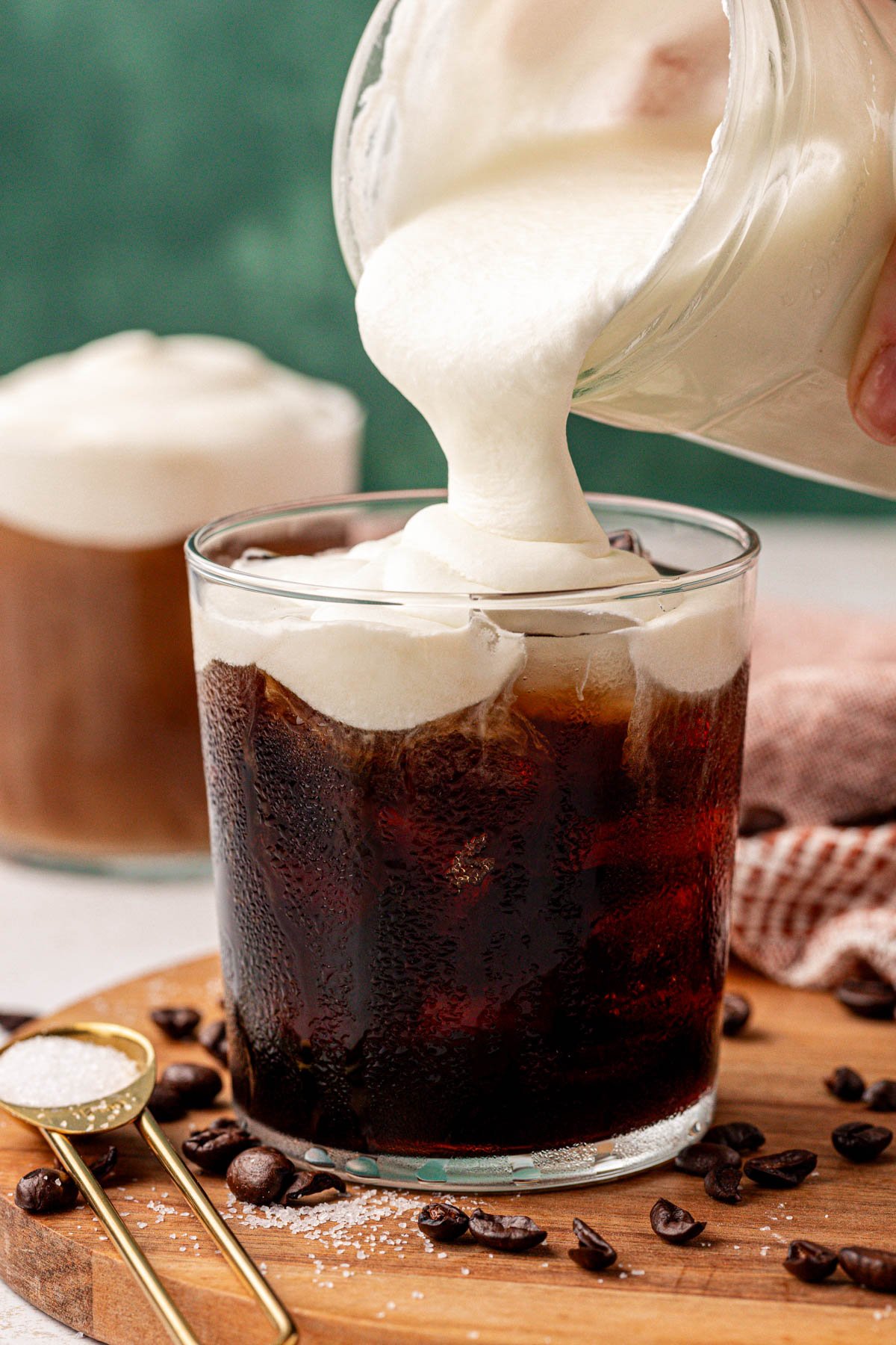 Cold foam being poured from a jar into a glass of cold brew.