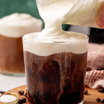 Cold foam being poured from a jar into a glass of cold brew.
