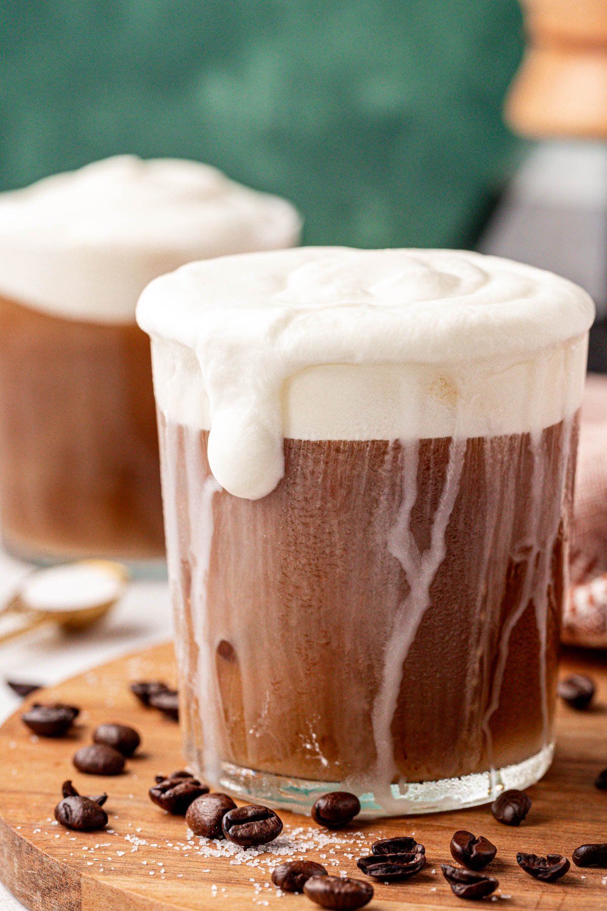 Close up of a glass of iced coffee with cold foam on a wooden tray.