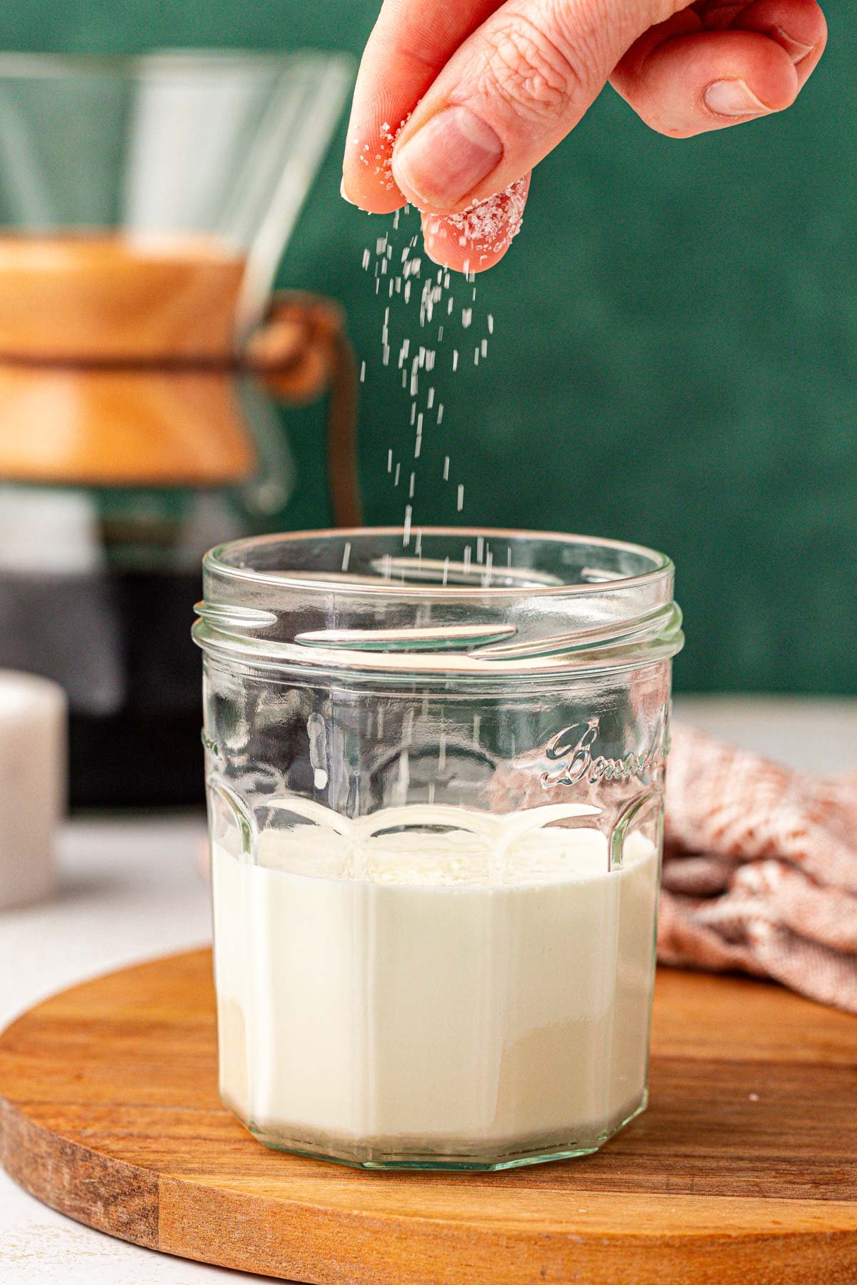 Salt being sprinkled into a jar of cream.