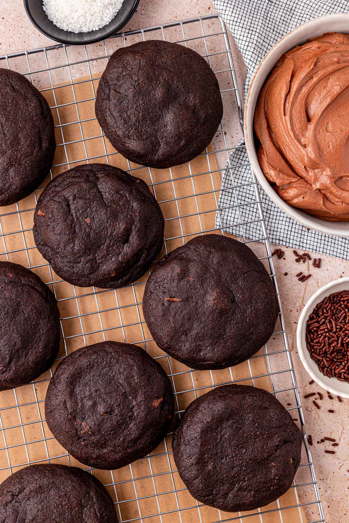 Chocolate cookies on a wire rack ready to be frosted with chocolate frosted from a nearby bowl.