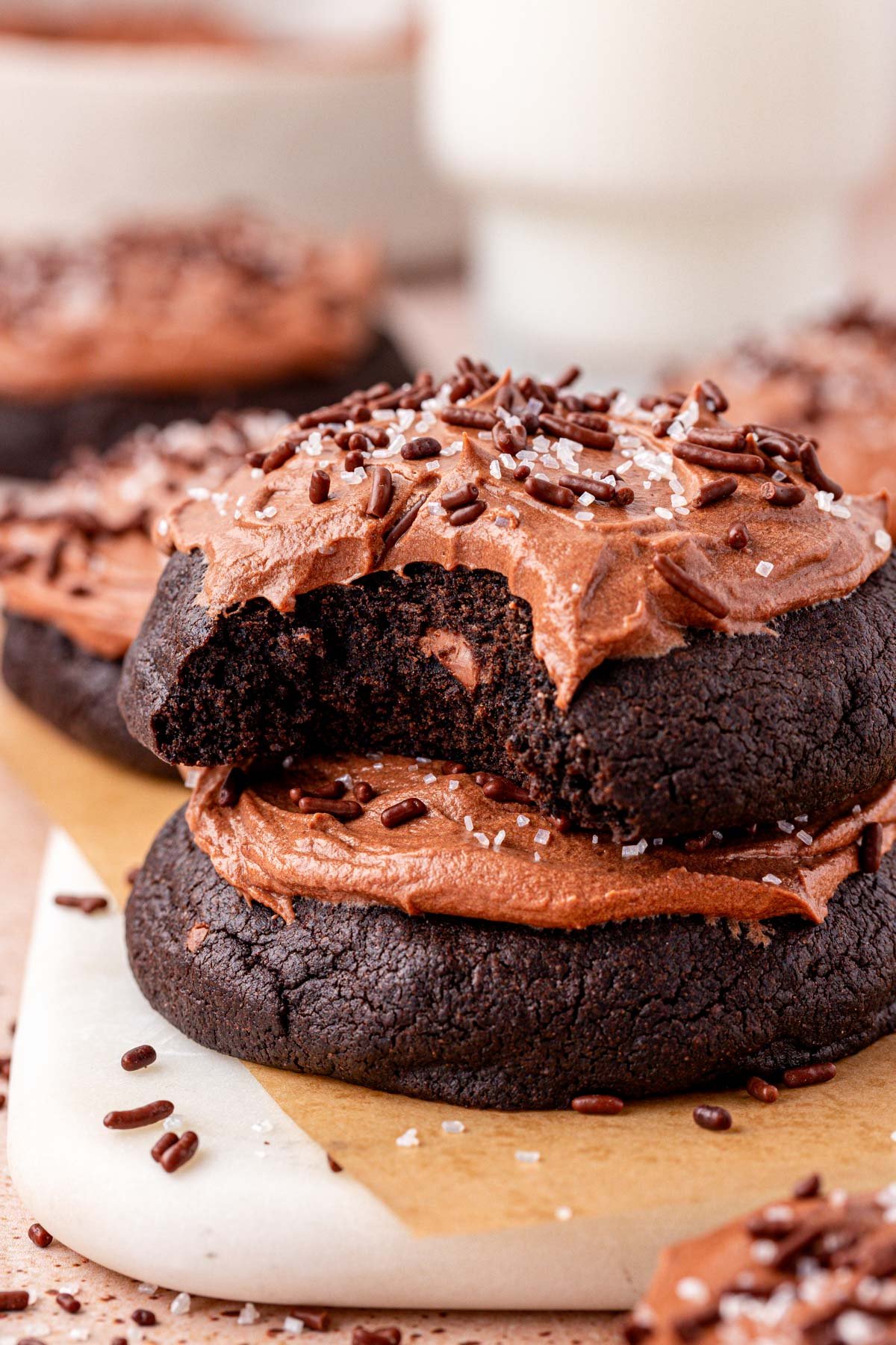 Two frosted chocolate cookies stacked on top of each other with the top one missing a bite.