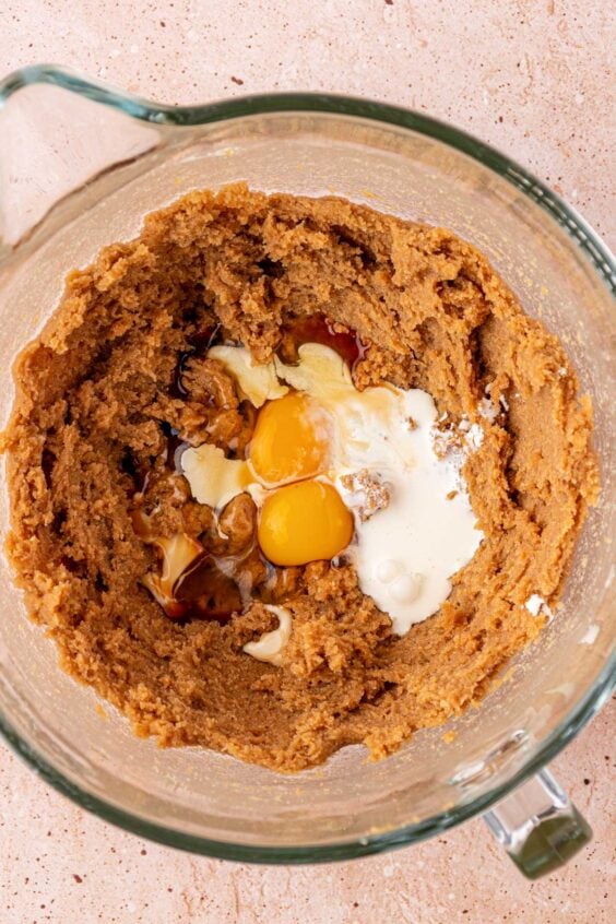 Cream and eggs being added to cookie dough in a stand mixer bowl.