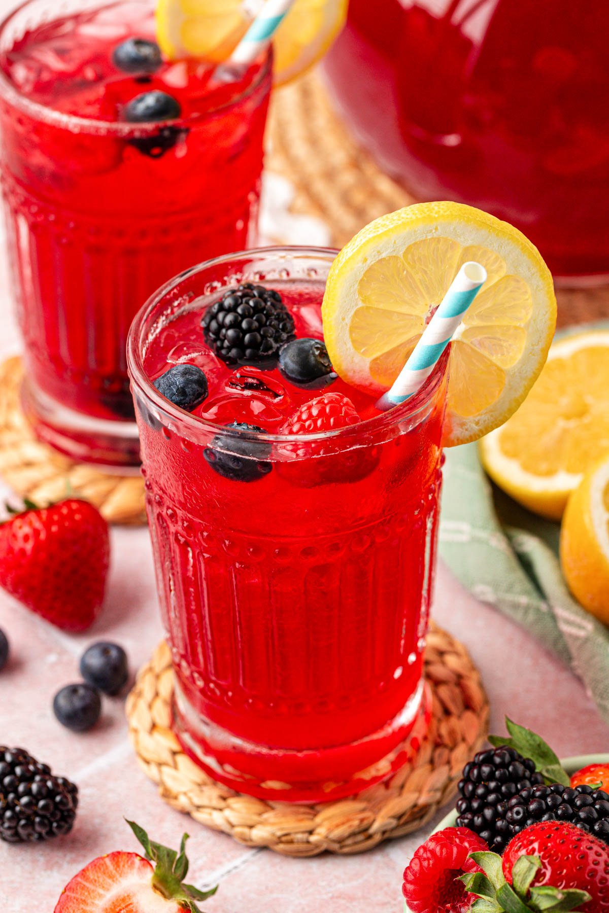 Close up of a glass filled with berry lemonade on a rattan coaster.