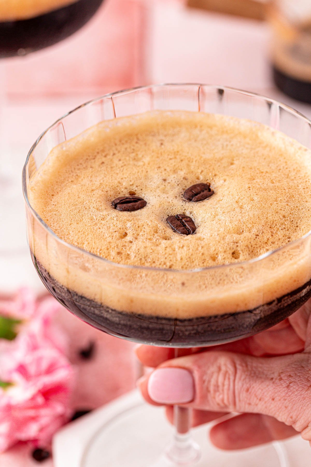 Close up of a woman's hand holding a coupe glass with a virgin espresso martini in it.