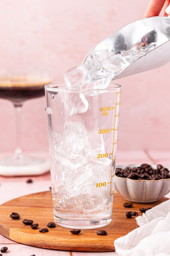 A scoop of ice being added to a cocktail shaker.